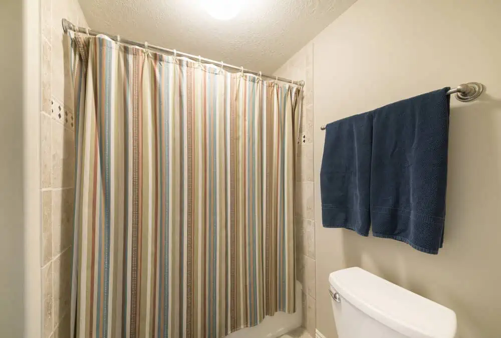 Colorful closed shower curtain in a windowless bathroom. There are two dark blue towels hanging on a towel bar above the toilet beside the curtain.