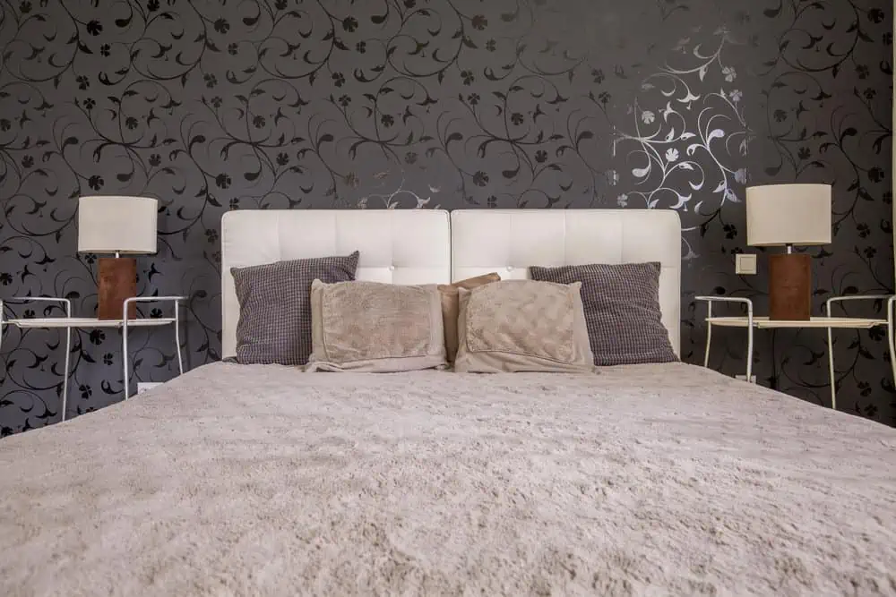 Dark bedroom with double bed, black pattern wallpaper, two nightstands and two small lamps