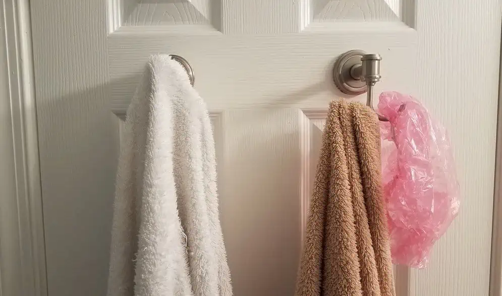 white and brown towel hanging on hooks on bathroom door with pink showercap